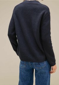 Pull texturé bleu marine avec un motif côtelé, coupe décontractée, épaules tombantes et manches longues, associé à un jean en denim bleu.