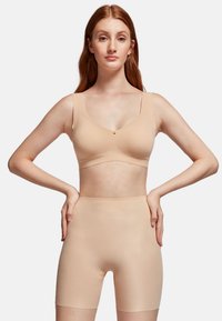 Beige seamless bra with wide straps and scoop neckline, paired with high-waisted, smooth-shaping shorts. Soft, stretchy fabric texture.