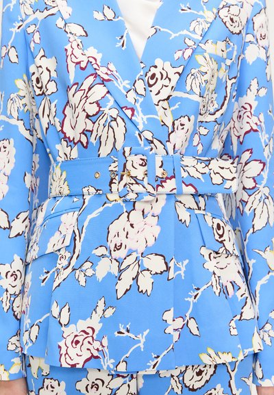 Blå blomsterprint blazer med en struktureret design, der har hvide og burgunderrøde blomster, en bæltestrop i taljen og en spids krave.