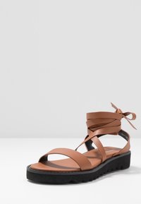 Ruske kožne sandale s više traka i omčom oko gležnja, koje imaju crnu teksturiranu podlogu i ravnu platformu.