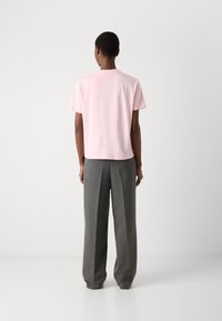 Light pink short-sleeve t-shirt with a rounded neckline, paired with high-waisted gray trousers with a textured finish and wide legs.