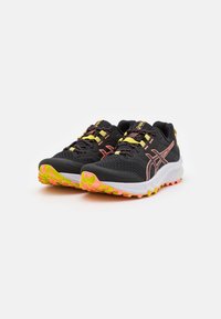Scarpe da atletica nere con tomaia in rete, caratterizzate da accenti gialli e rosa, una suola intermedia spessa bianca e una suola esterna multicolore texturizzata.