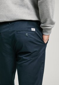 Námořnické modré lehké kalhoty se zadní kapsou se zapínáním na knoflík a malou značkovou nášivkou. Hladká tkanina a přiléhavý střih.