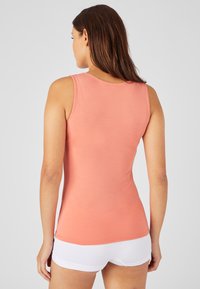 Top rosa con collo rotondo e design senza maniche, realizzato in tessuto morbido. Indossato con pantaloni corti bianchi, che mostrano una silhouette aderente.