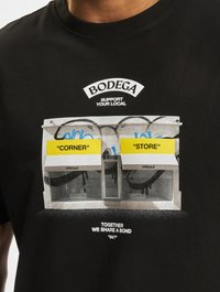 Sort bomulds t-shirt med et grafisk design af to åbne butikker med gule skilt, der står "CORNER" og "STORE," samt tekst nedenfor.