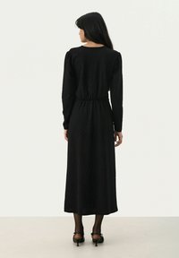 Langes schwarzes Kleid aus strukturiertem Stoff mit langen Ärmeln und einer taillierten Passform mit einem elastischen Bund. Glatter Saum und einfarbig.