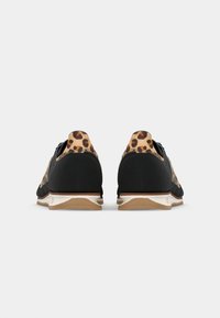 Black sneakers with leopard print accents, textured material, rounded heel, and contrasting white outsole. Low-profile design with lace closure.