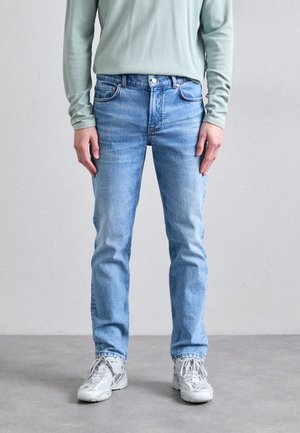 Ljust blå denimjeans med rak passform, femficksdesign, subtil blekning och knäppning, kombinerat med vita sneakers och en långärmad skjorta.