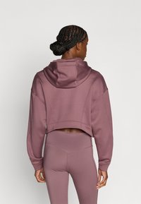 Korte hoodie in mauve, met lange mouwen, geribbelde boorden en naden. Gecombineerd met hoge taille legging in dezelfde kleur.