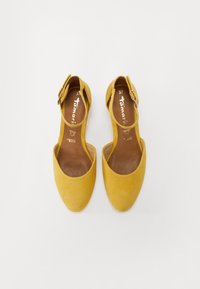 Ballerines en suède jaune avec un bout pointu, des côtés ouverts et une sangle à la cheville réglable. La semelle intérieure est marron avec un logo doré. Taille 37.