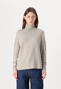 Beige turtleneck neule pehmeässä tekstuurissa, pitkät hihat, rento malli ja hieman lyhyempi helma, yhdistetty tummansinisiin farkkuihin.