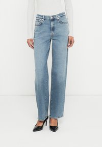 Kõrge vöökohaga helesinised teksad sirge säärega, viie tasku ja õrna tuhmumisega. Sobitatud mustade teravate kannastega.