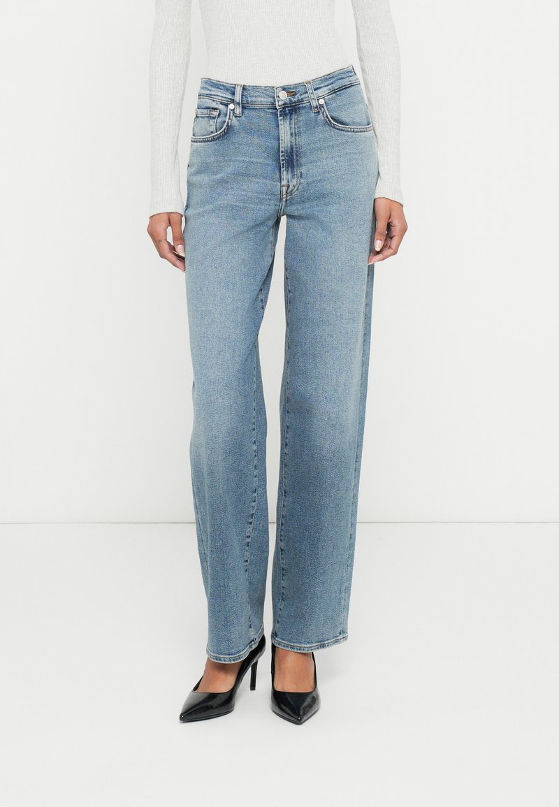 Kõrge vöökohaga helesinised teksad sirge säärega, viie tasku ja õrna tuhmumisega. Sobitatud mustade teravate kannastega.