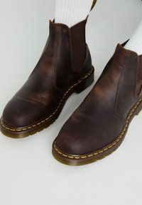 Bruna läder Chelsea-boots med elastiska sidopaneler, gul sömnad och en texturerad sula. Designen har en rundad tå och en slät yta.