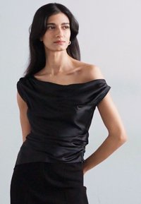 Top din satin negru, cu umeri descoperiți, design drapat, croială slim și ușoară adunare la talie. Textură fină și detalii minime accentuează eleganța.