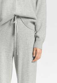 Grau gestrickter Pullover mit lockerer Passform, langen Ärmeln und gerippten Bündchen. Kordelzugdetail an der Taille mit passenden grauen Hosen. Weicher Stoff.