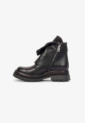 Bottine noire en cuir avec semelle épaisse, fermeture éclair latérale partiellement ouverte et rabat en cuir plié sur le devant.