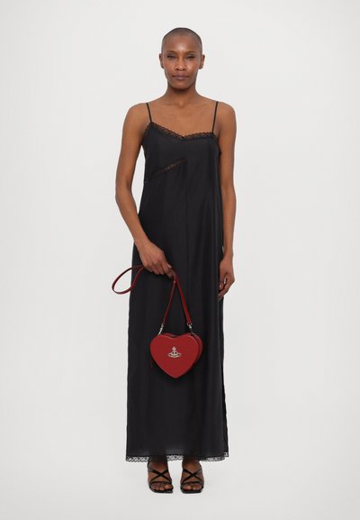 Abito sottoveste nero con pizzo, dotato di spalline regolabili, abbinato a una borsa a forma di cuore rossa con logo. Sandali neri con cinturini completano il look.
