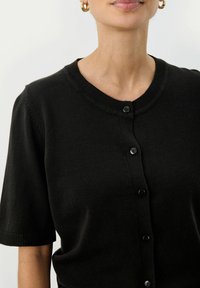 Schwarze kurzärmelige Strickjacke mit Rundhalsausschnitt, ausgestattet mit einer Knopfleiste und gerippten Details. Glatte Textur und minimalistisches Design.