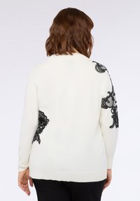 Weißer Pullover mit schwarzer Spitze an Schultern und Seiten, aus weichem Material und mit langen Ärmeln, konzipiert für einen lässigen Schnitt.