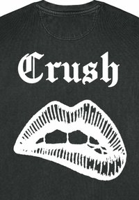 T-shirt nera con il testo bianco in grassetto "Crush" e una grafica dettagliata di labbra con motivi a linee, evidenziando i contorni e la texture.