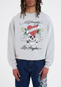 Grå sweatshirt med et farverigt grafisk motiv med et kranium, et hjerte, og teksten "Love Kills Slowly" og "Los Angeles." Langærmet, afslappet pasform.