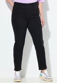 Los pantalones de mezclilla negros tienen un diseño de pierna recta, bolsillos frontales y una cinturilla clásica con cierre de botón. Se llevan con zapatillas multicolor.