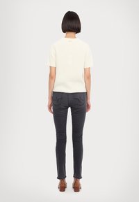 Top corto a maniche corte in maglia bianca a coste abbinato a jeans fitted grigio scuro. Modella che indossa sandali con tacco marroni, vista da dietro.