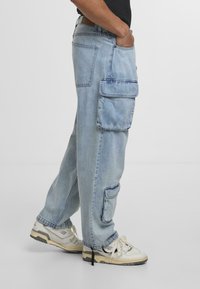 Lysblå denim cargo bukser med overdimensionerede lommer, afslappet pasform og manchetter. Båret med hvide sneakers med sorte detaljer.