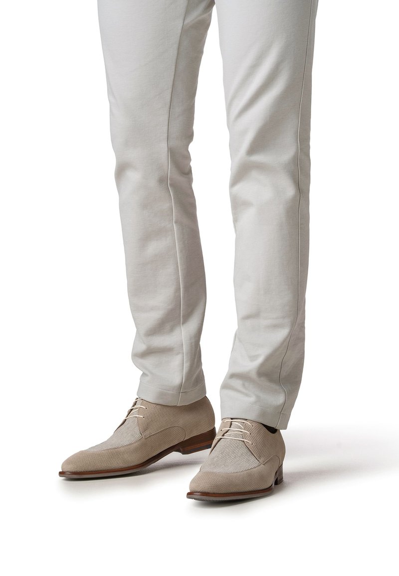 Chaussures habillées beiges texturées avec un bout lisse et un design en tissu mixte, accompagnées d'un pantalon ajusté de couleur claire.