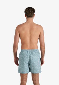 Lichtblauwe zwembroek met een wit bladerenpatroon, elastische tailleband en een achterzak. Het materiaal lijkt lichtgewichtig en ademend te zijn.