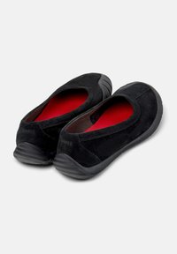 Scarpe slip-on in suede nero con interno rosso e suole in gomma nera testurizzata, caratterizzate da una punta arrotondata e dettagli di cucitura minimi.