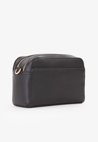 Schwarze Kosmetiktasche mit glatter, strukturiertem Oberfläche, doppelten Reißverschlüssen und rechteckiger Form mit abgerundeten Kanten.