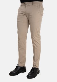 Chino beige in cotone. Design slim fit con una texture liscia. Presenta una chiusura a bottone e tasche laterali. Abbinato a scarpe nere con lacci.