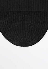 Black knitted rug with a ribbed texture and rounded edges, featuring a soft, dense material. The design shows subtle variations in weave.