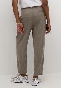 Bézs, egyenes szabású, testre szabott nadrág két hátsó zsebbel és sima textúrával, ezüst sportcipővel párosítva.