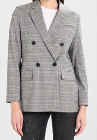 Blazer doppiopetto a fantasia grigia a quadri con bottoni neri, dotato di due tasche frontali e rever a punte. Texture morbida, design strutturato.