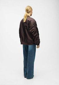 Brun satin bomberjakke med gatherede ærmer, ribbede manchetter og kant, parret med oversized blå denimjeans.