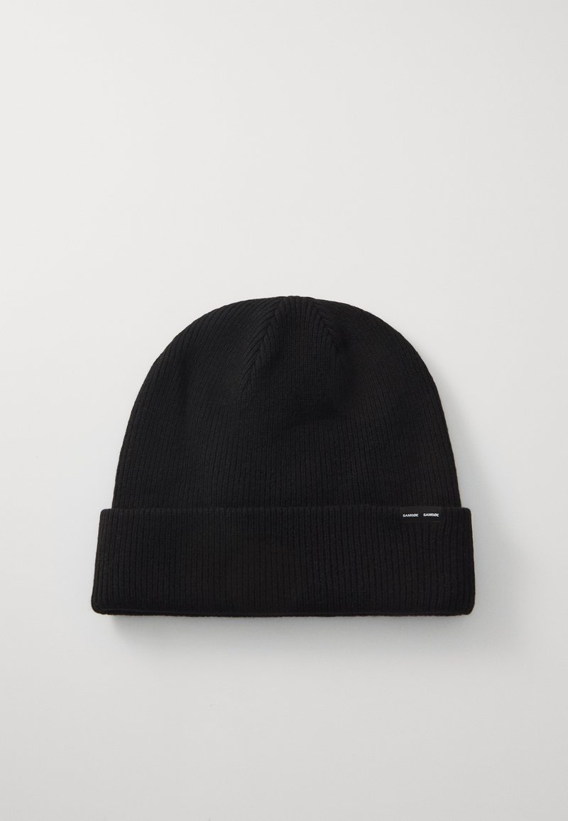 Black knitted beanie with a ribbed texture. Folded cuff design features small white tags. Made from a soft, stretchy material suitable for warmth.