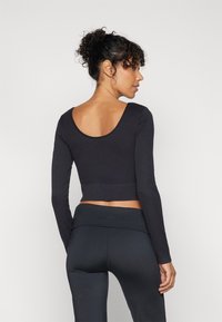 Crni dugoruki crop top s zaobljenim izrezom na leđima i priljubljenim dizajnom, uparen s crnim tajicama visokog struka. Glatka tekstura.