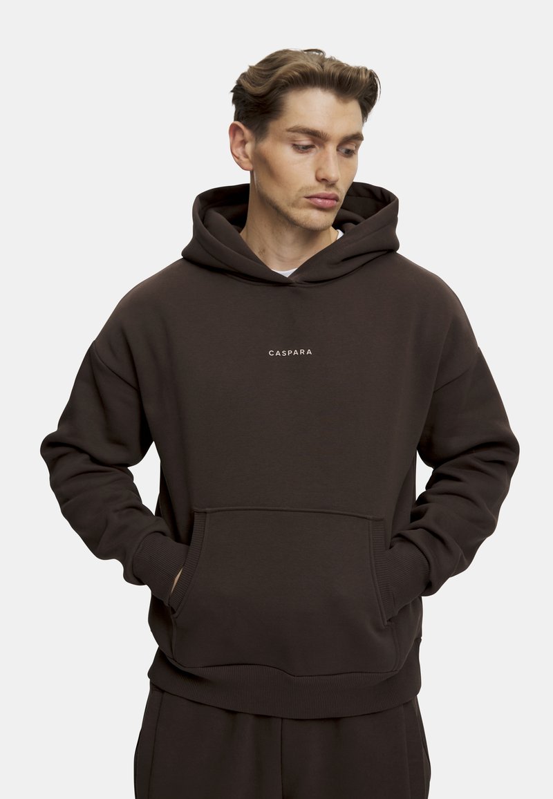 Mørkebrun hettegenser laget av mykt stoff, med kengurulomme, ribbede mansjetter og en liten hvit logo "CASPARA" på brystet.