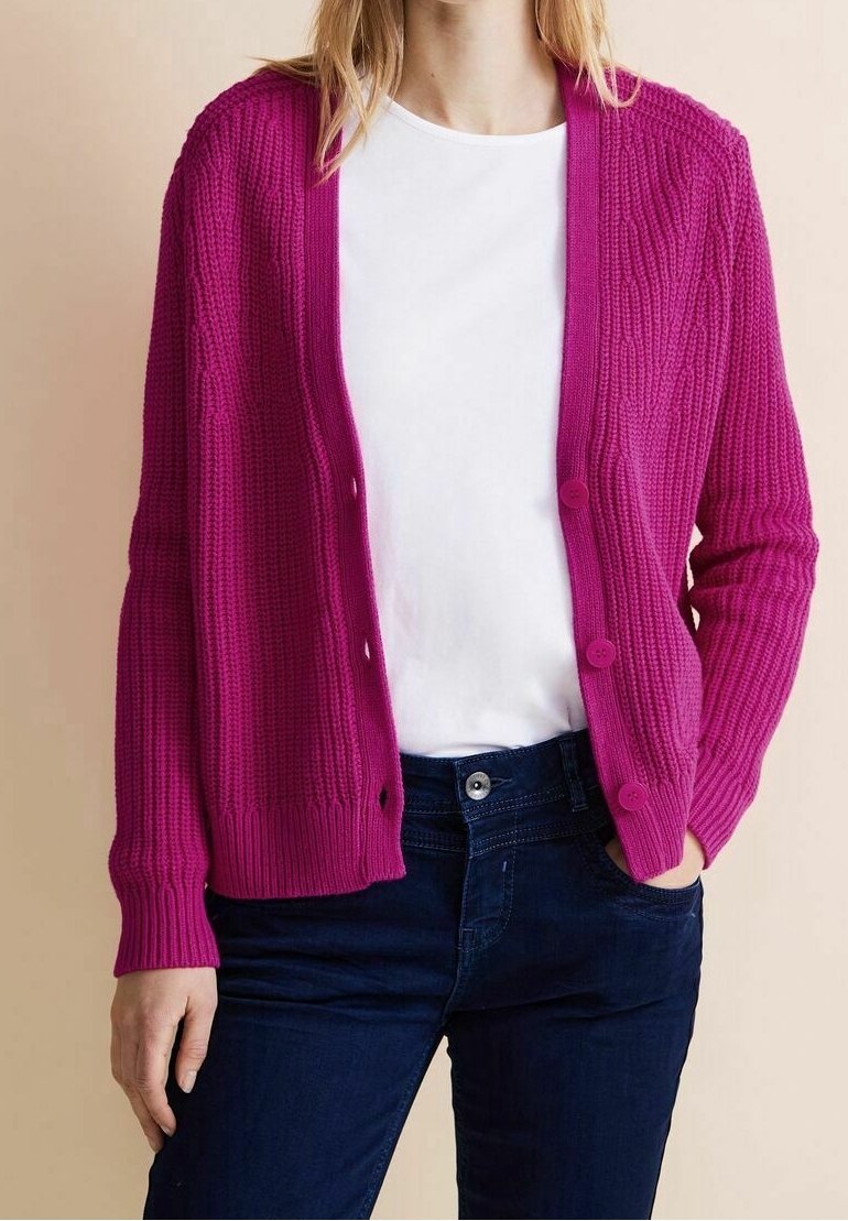 Fuchsia stickad cardigan med långa ärmar, ribbad textur och framknappar, bärs över en vit skjorta och mörk jeans.