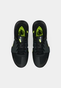 Μαύρα αθλητικά παπούτσια με υφή από διχτυωτό ανώτερο μέρος, νέον πράσινες λεπτομέρειες και ανακλαστικά στοιχεία. Στρογγυλεμένη ελαστική σόλα για πρόσφυση και υποστήριξη.