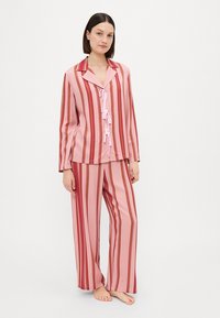Gestreepte roze pyjama set met een button-up top voorzien van een kraag, manchetten en een kanten strikdetail, gecombineerd met bijpassende losse broek.