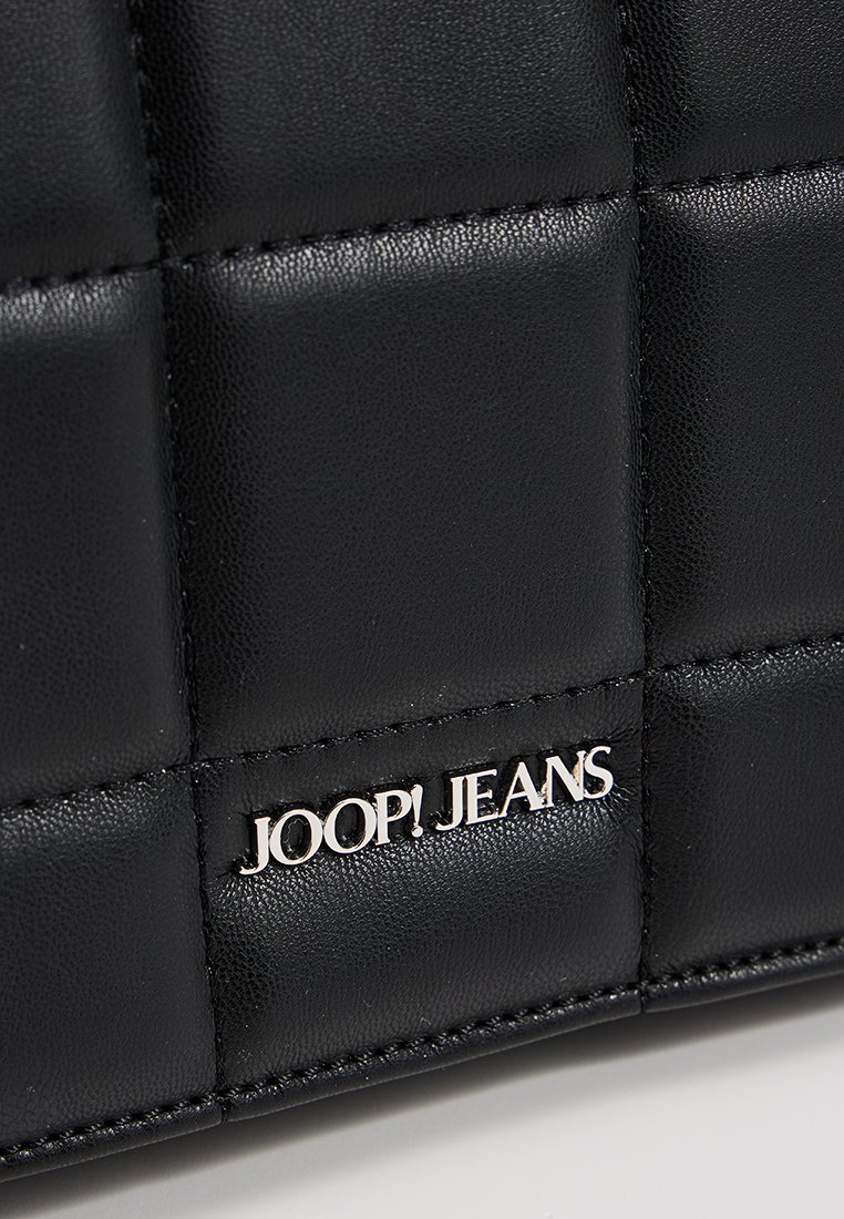 Zbliżenie na czarną pikowaną skórzaną powierzchnię z przywieszką z logo "JOOP! JEANS" w kolorze srebrnym.