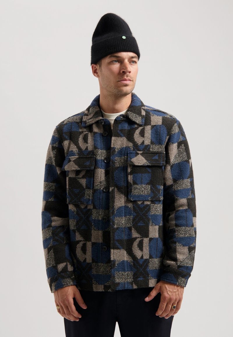 Plaid shirt jacket in a woven fabric featuring blue, black, and gray geometric patterns, with button closure and two front pockets.