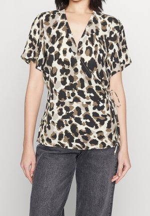 Vrouw draagt een korte mouw, V-hals luipaardprint wikkelblouse gestrikt in de taille, gecombineerd met donkergrijze spijkerbroek.