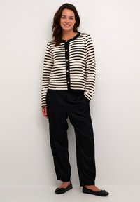 Cardigan în dungi, de culoare crem și bleumarin, cu guler rotund și nasturi aurii; asortat cu pantaloni negri lejeri și balerini negri. Textură netedă.