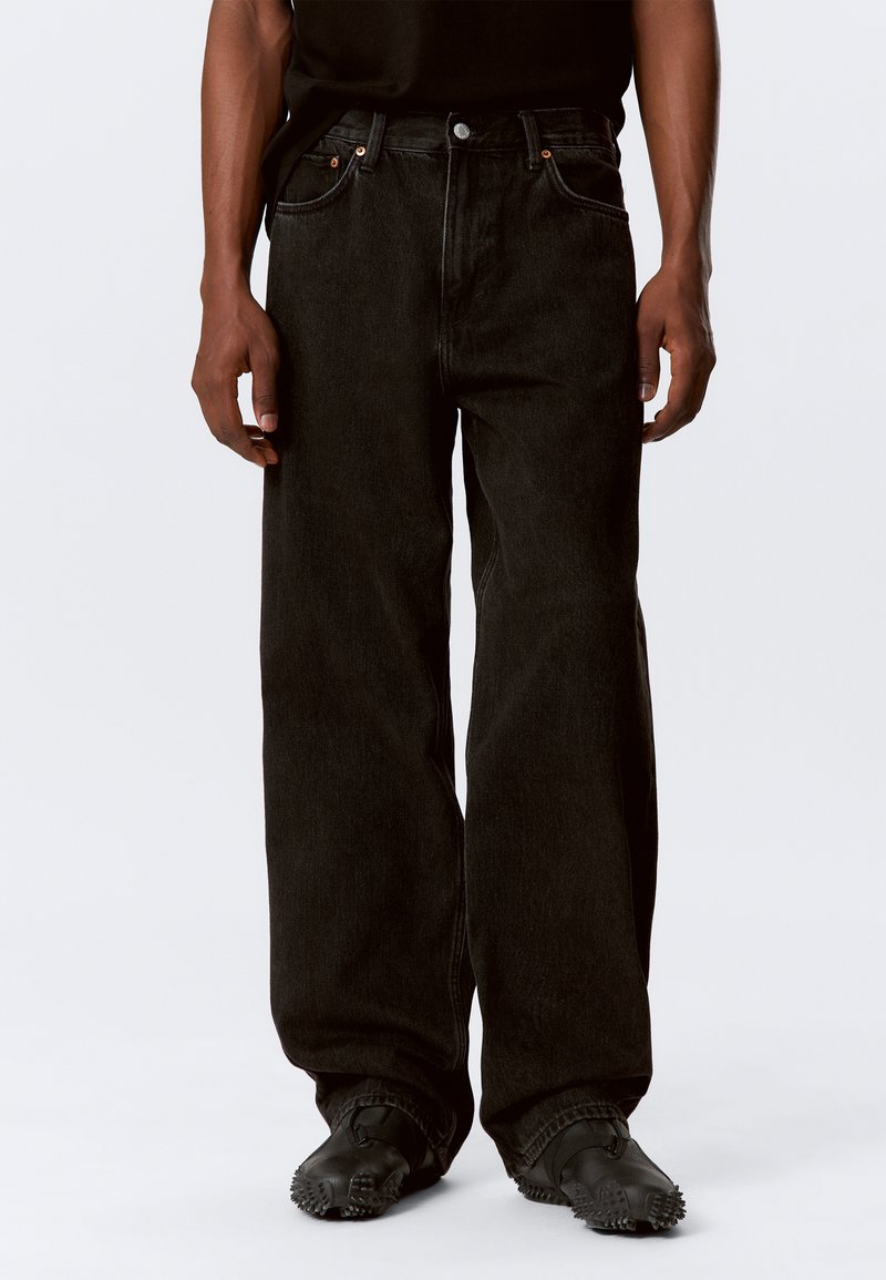 Black oversized denim jeans with a straight leg, five-pocket design, and subtle textured fabric. Metallic hardware accents near pockets.