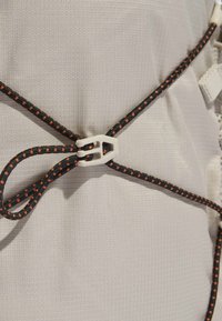 Corda elastica nera e arancione fissata con una clip di plastica bianca su uno sfondo di tessuto chiaro e testurizzato.